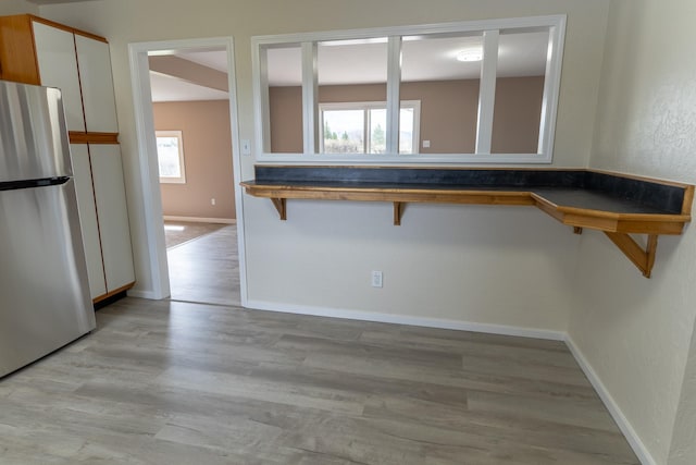kitchen with a breakfast bar, freestanding refrigerator, baseboards, light wood-style flooring, and white cabinetry