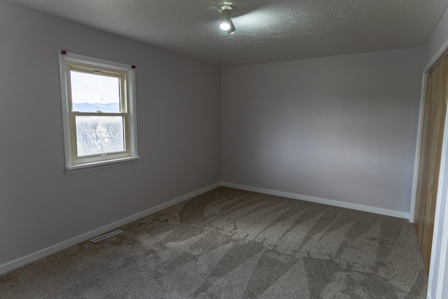 carpeted empty room with baseboards, a textured ceiling, and visible vents
