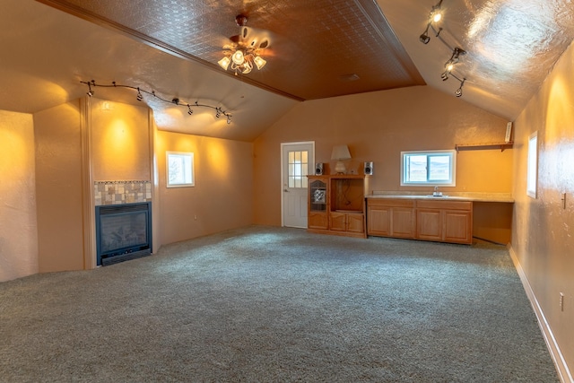 unfurnished living room with track lighting, lofted ceiling, a tile fireplace, and carpet