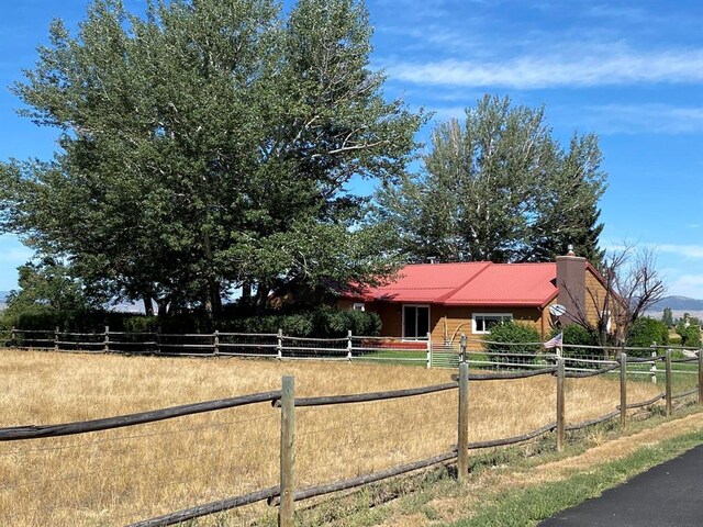 view of front of property with fence, a rural view, a chimney, and metal roof