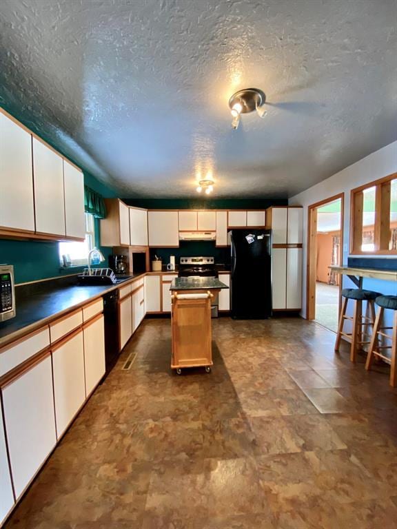 kitchen featuring a center island, black appliances, white cabinets, sink, and a textured ceiling