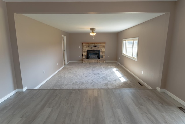 unfurnished living room with a stone fireplace, baseboards, and wood finished floors