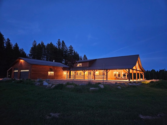 back house at dusk featuring a garage and a lawn