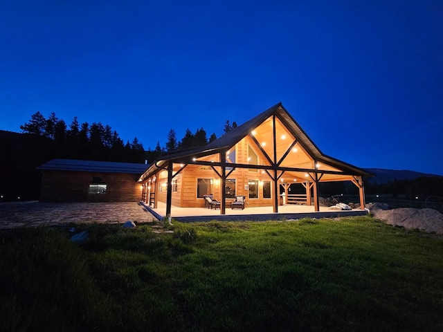 back house at twilight featuring a lawn and a patio