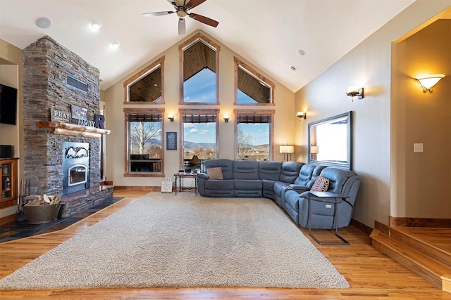 living room with light wood-type flooring, high vaulted ceiling, a stone fireplace, and ceiling fan