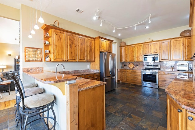 kitchen with a kitchen bar, appliances with stainless steel finishes, kitchen peninsula, decorative backsplash, and pendant lighting