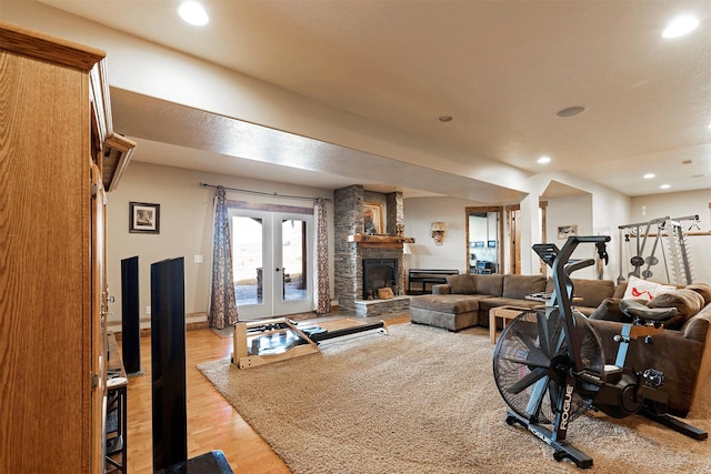 workout area featuring french doors, light hardwood / wood-style floors, and a stone fireplace