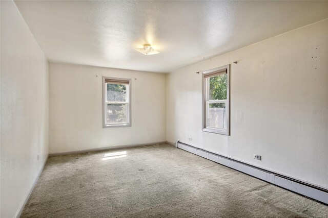 carpeted empty room with a healthy amount of sunlight and a baseboard heating unit