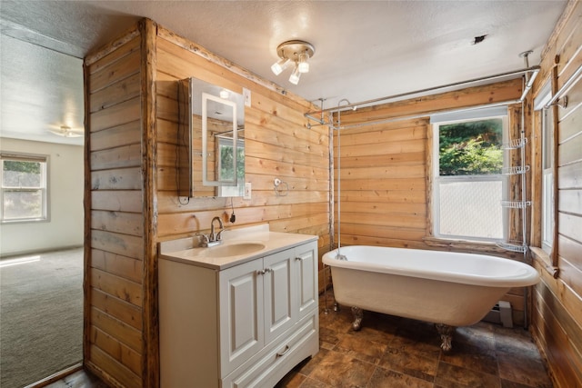 bathroom featuring a washtub, a textured ceiling, vanity, and wooden walls