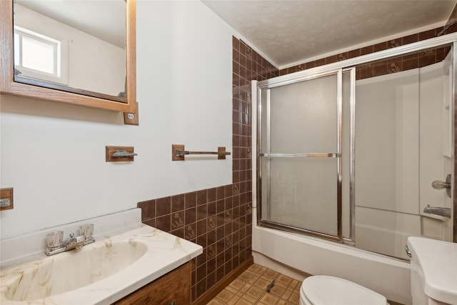 full bathroom with vanity, toilet, bath / shower combo with glass door, and tile walls