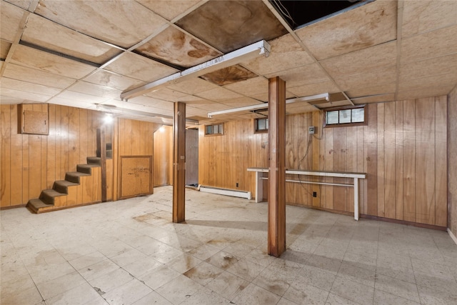 basement with a paneled ceiling, a baseboard heating unit, and wood walls