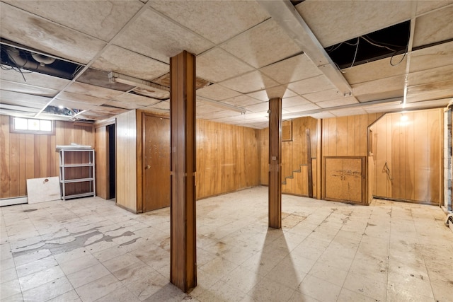 basement with a baseboard heating unit, a paneled ceiling, and wooden walls