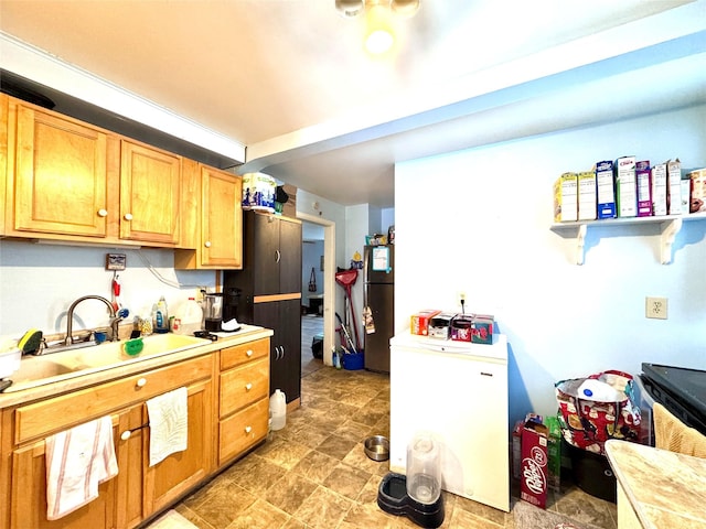 kitchen with brown cabinets, refrigerator, freestanding refrigerator, light countertops, and a sink