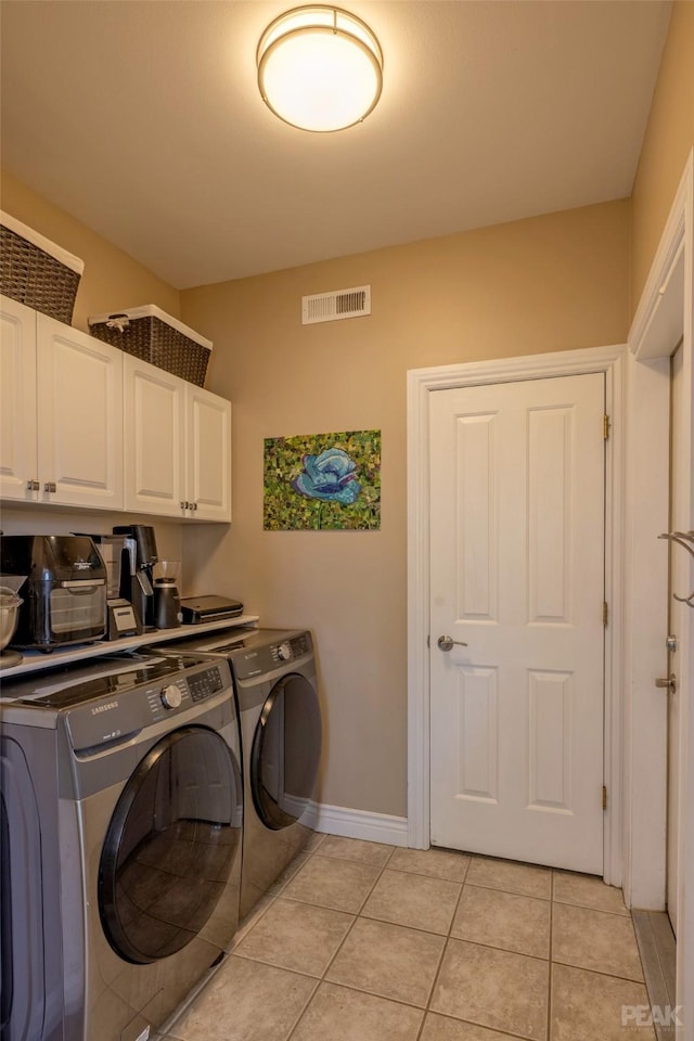 laundry room featuring washing machine and clothes dryer, light tile patterned floors, and cabinets