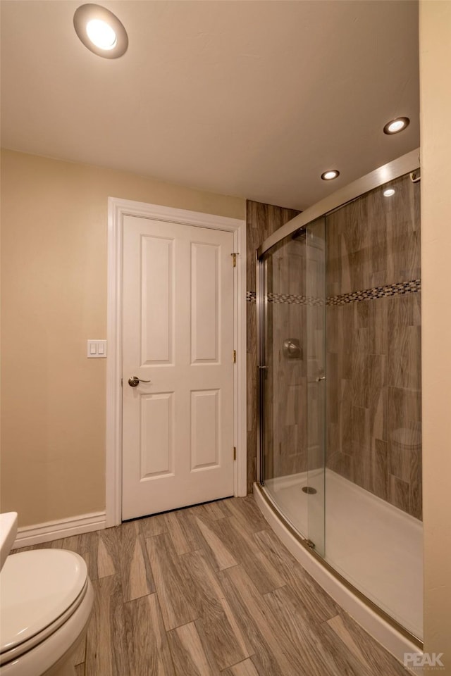 bathroom featuring wood-type flooring, toilet, and a shower with door