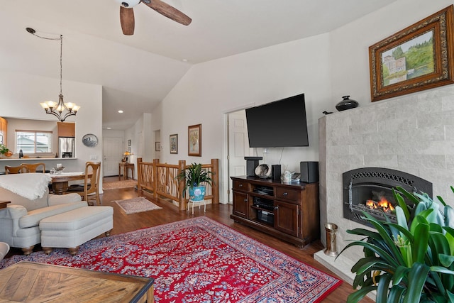 living room with ceiling fan with notable chandelier, dark hardwood / wood-style floors, vaulted ceiling, and a tile fireplace