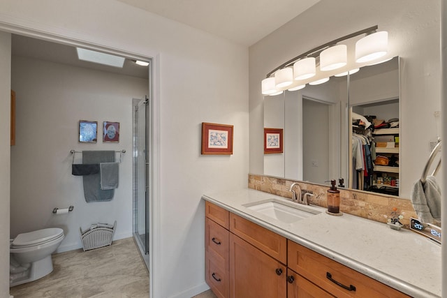 bathroom featuring a skylight, vanity, toilet, and a shower with shower door