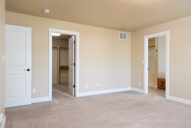 unfurnished bedroom with ensuite bathroom, a walk in closet, light carpet, and a closet