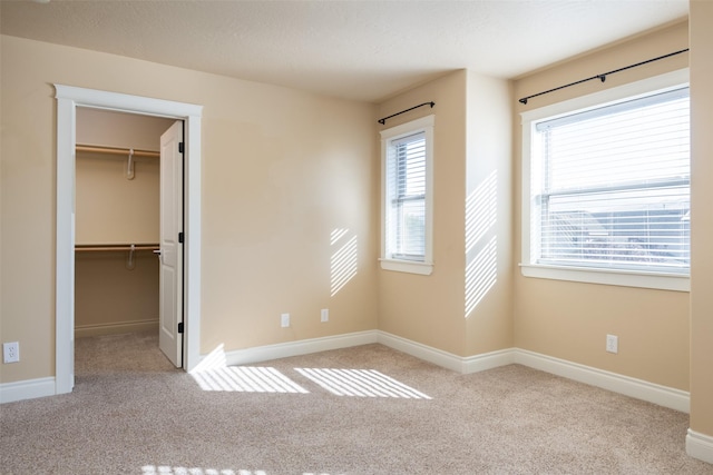 unfurnished bedroom with a walk in closet, a closet, and light colored carpet