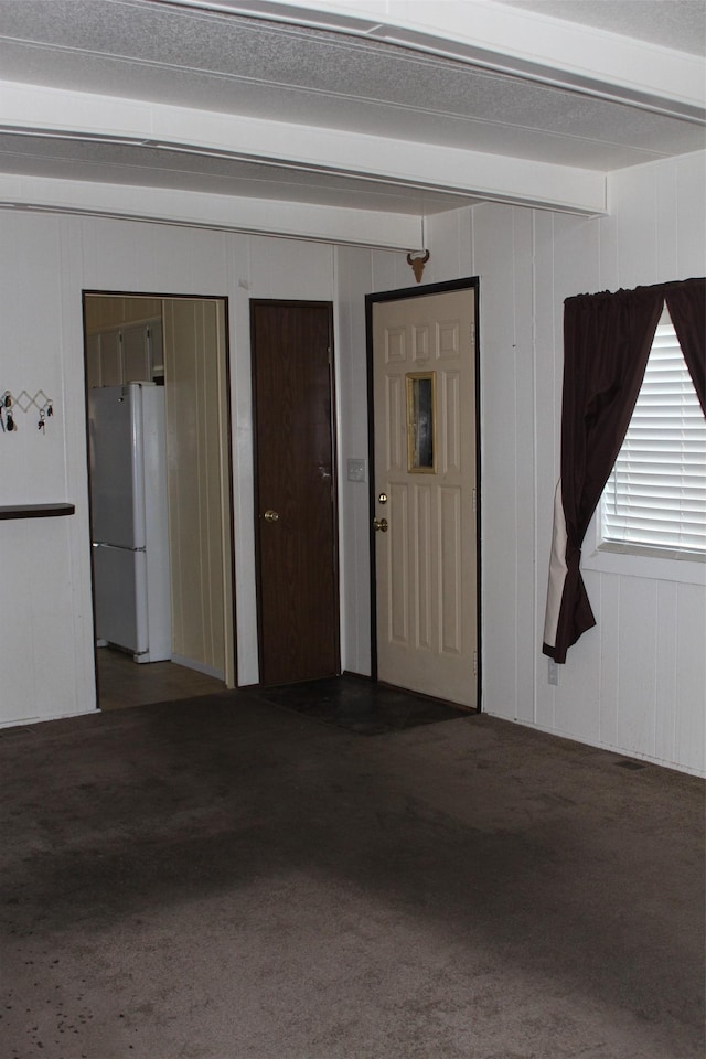 carpeted spare room with beam ceiling and wood walls