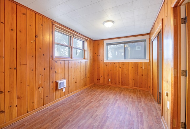 unfurnished room featuring light hardwood / wood-style floors, wooden walls, and a wall mounted AC