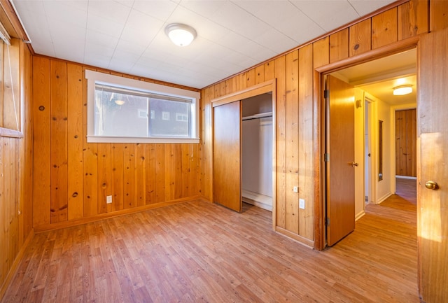 unfurnished bedroom with wooden walls, a closet, and light hardwood / wood-style flooring