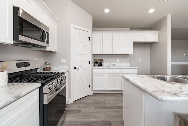 kitchen featuring light stone counters, white cabinetry, appliances with stainless steel finishes, and light hardwood / wood-style flooring