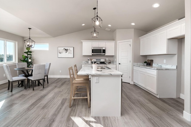 kitchen featuring light stone countertops, appliances with stainless steel finishes, a kitchen island with sink, pendant lighting, and white cabinets