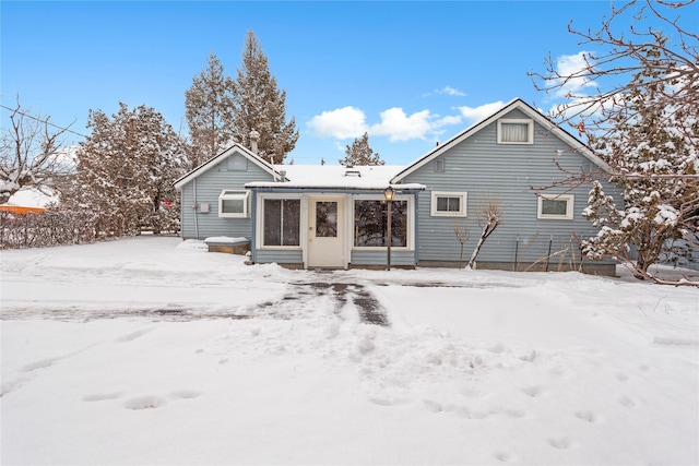 snow covered rear of property featuring a sunroom