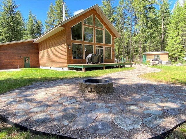 rear view of property featuring a fire pit, a shed, a deck, and a lawn