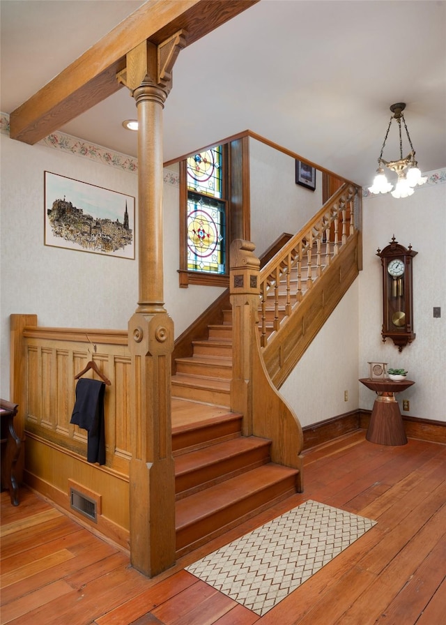 stairs featuring hardwood / wood-style floors, an inviting chandelier, and beam ceiling