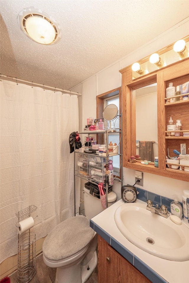 bathroom with vanity, a textured ceiling, toilet, and walk in shower