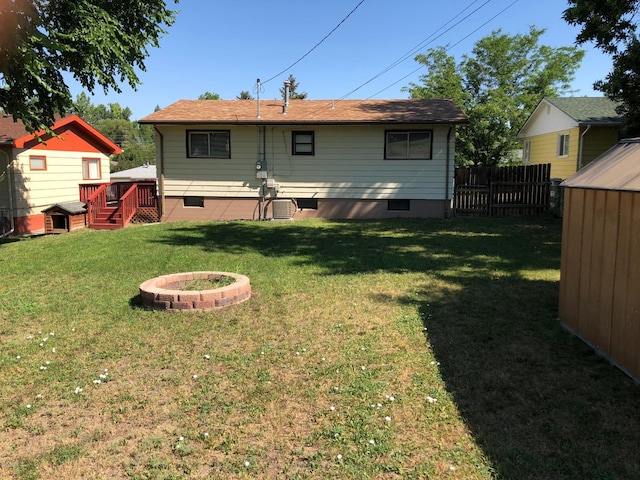 back of house with a fire pit, a wooden deck, and a lawn