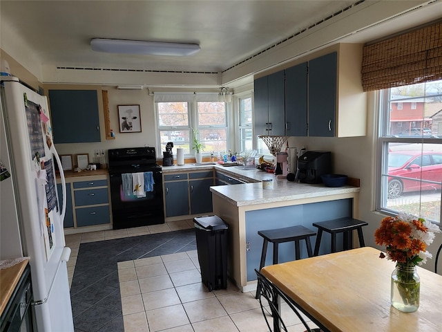 kitchen with kitchen peninsula, a wealth of natural light, light tile patterned floors, white fridge, and black electric range oven