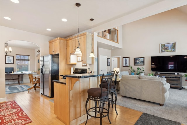 kitchen with a kitchen breakfast bar, hanging light fixtures, stainless steel fridge, light wood-type flooring, and kitchen peninsula