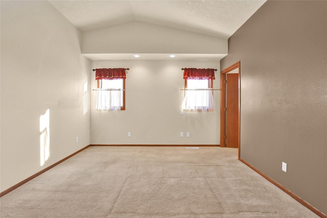 spare room with light carpet, plenty of natural light, and vaulted ceiling