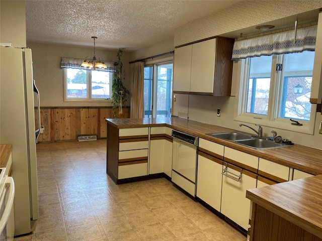 kitchen with sink, hanging light fixtures, fridge, white dishwasher, and kitchen peninsula