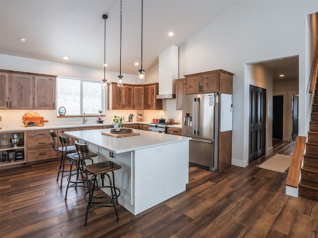 kitchen with premium appliances, decorative light fixtures, high vaulted ceiling, wall chimney range hood, and a center island