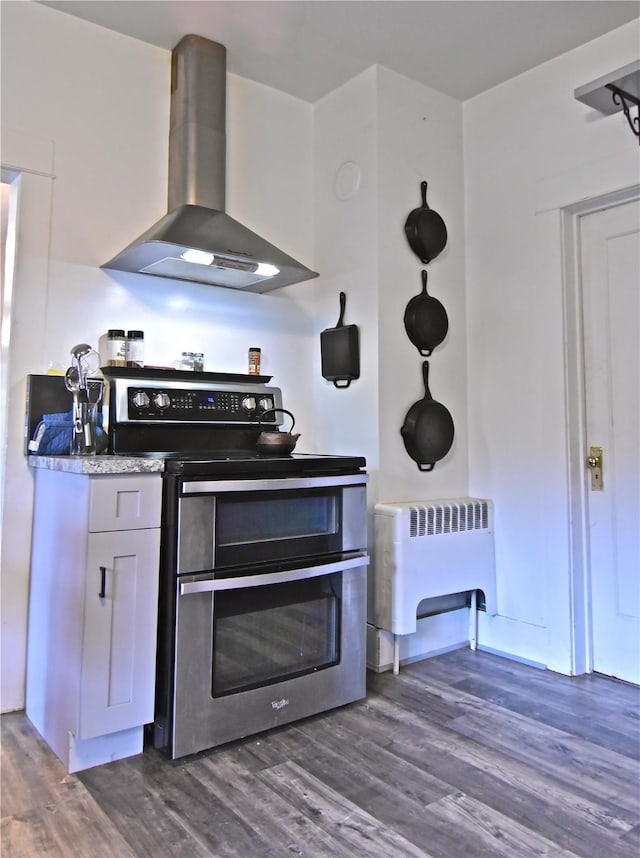 kitchen featuring dark hardwood / wood-style flooring, radiator, wall chimney exhaust hood, electric range, and white cabinets