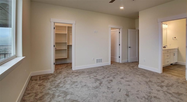 unfurnished bedroom featuring light carpet, a walk in closet, ensuite bath, ceiling fan, and a closet