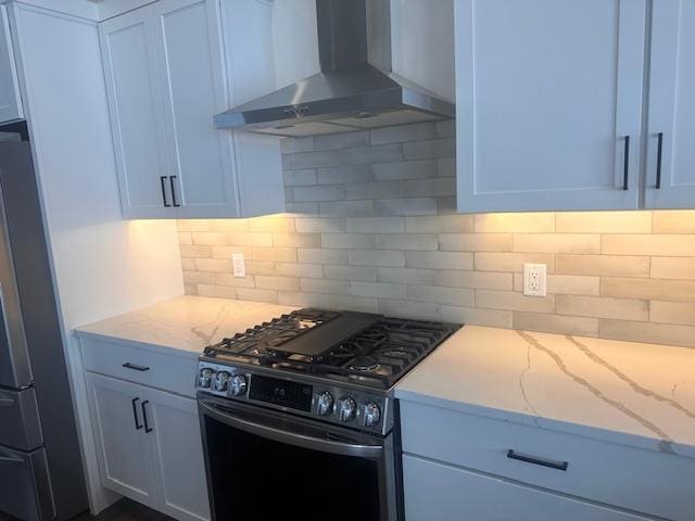 kitchen with black gas range, white cabinetry, wall chimney range hood, tasteful backsplash, and stainless steel fridge