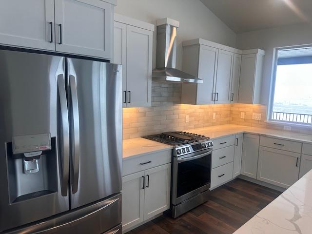 kitchen featuring white cabinets, stainless steel appliances, light stone counters, and wall chimney range hood