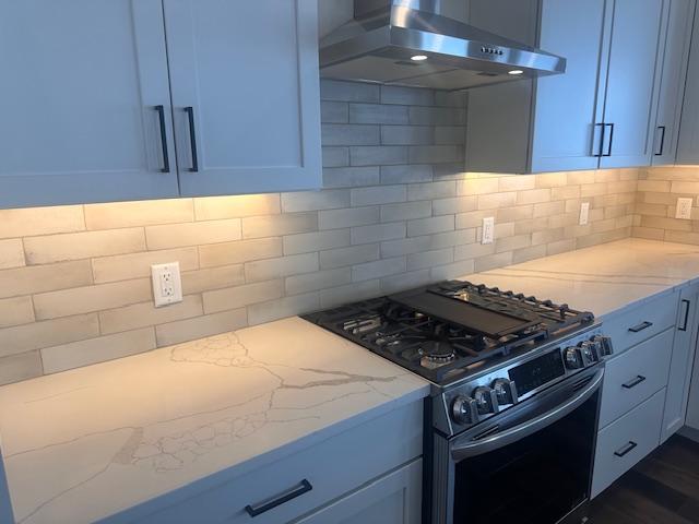 kitchen with decorative backsplash, black gas stove, light stone countertops, and wall chimney exhaust hood