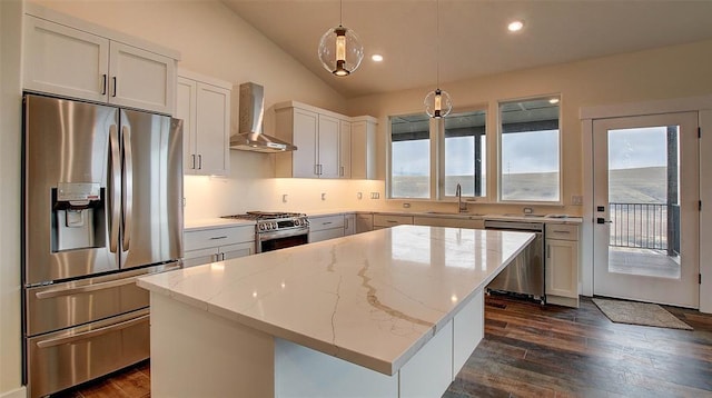 kitchen featuring white cabinetry, hanging light fixtures, stainless steel appliances, wall chimney range hood, and a kitchen island