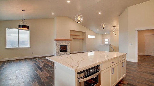 kitchen featuring a center island, oven, decorative light fixtures, light stone counters, and white cabinetry