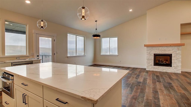 kitchen with light stone countertops, a stone fireplace, decorative light fixtures, a kitchen island, and appliances with stainless steel finishes