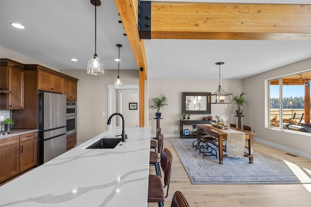 kitchen featuring hanging light fixtures, light stone countertops, sink, and stainless steel appliances