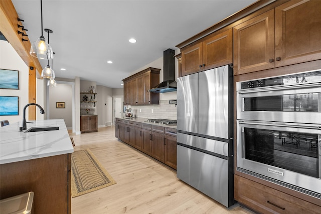 kitchen featuring appliances with stainless steel finishes, light stone counters, sink, wall chimney range hood, and pendant lighting