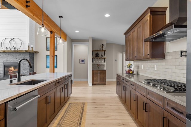 kitchen featuring sink, stainless steel appliances, wall chimney range hood, decorative light fixtures, and a fireplace