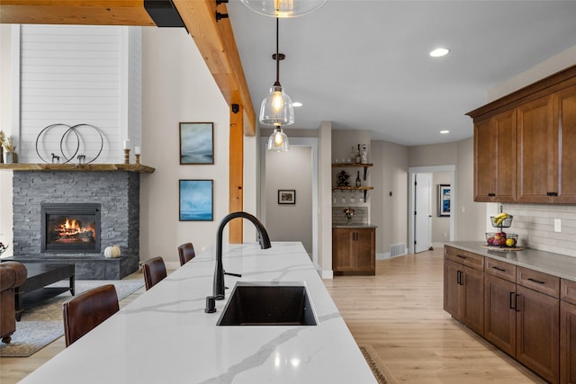 kitchen featuring sink, light stone counters, light hardwood / wood-style flooring, decorative light fixtures, and a fireplace